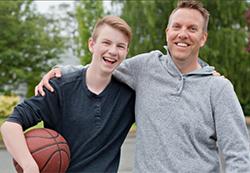 Man with his arm around shoulder of a teenage boy holding basket ball