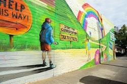 Colourful mural on brick wall showing a path to a rainbow with signs "Help this way" and "Start a conversation".