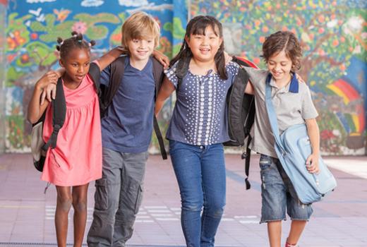 Children walking arm in arm with school bags 
