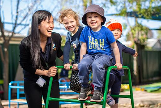 3 young children in laughing in playground with a teacher