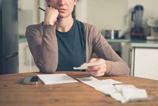 Woman looking concerned over a several receipts.  Holding a pen.  Note pad on the table.
