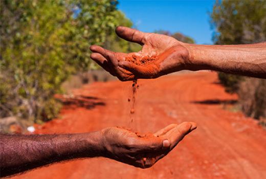 Open palms of two people's hands dripping crumbling red soil 
