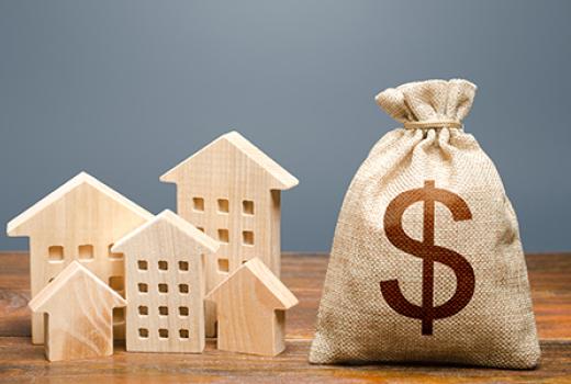Wooden blocks in shapes of houses and building next to a sack with a dollar sign