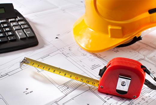 Building plans, industrial tape measure, hard hat and calculator