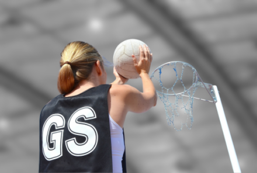 Girl wearing bib with GS on her back preparing to shoot for a netball goal