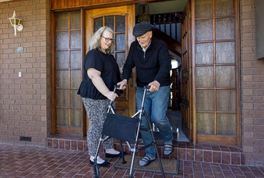 Man using a walker being assisted to walk down front door step