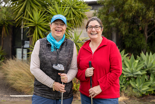 Two women smiling and holding golf clubs