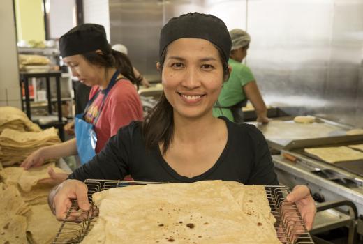 A women in a black bakers outfit holding a tray of roti bread.